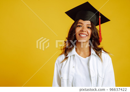 Portrait of African American woman in a graduation hat on her head posing on a yellow background. Portrait of African American woman in a graduation hat on her head posing on a yellow background. 96637422