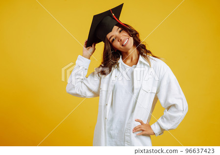 Portrait of African American woman in a graduation hat on her head posing on a yellow background. 96637423
