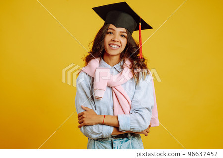Graduate woman in a graduation hat on her head posing on a yellow background. Study, education, university, college, graduate concept. 96637452