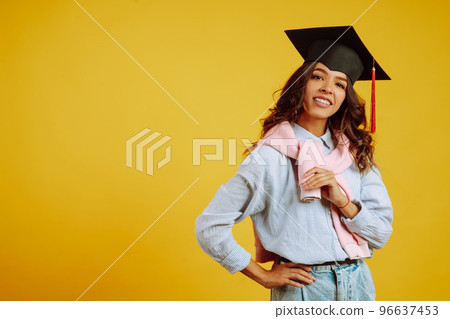 Graduate woman in a graduation hat on her head posing on a yellow background. Study, education, university, college, graduate concept. Graduate woman in a graduation hat on her head posing on a yellow background. Study, education, university, college, graduate concept. 96637453