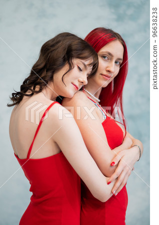 A close-up portrait of two tenderly embracing women dressed in identical red dresses. Lesbian intimacy. 96638238