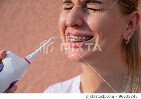 A woman with braces on her teeth uses an irrigator. Close-up portrait. A woman with braces on her teeth uses an irrigator. Close-up portrait. 96638245
