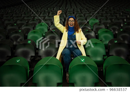 Caucasian woman cheers for a sports team at the stadium. The girl watches the match at the stadium alone. Caucasian woman cheers for a sports team at the stadium. The girl watches the match at the stadium alone. 96638537