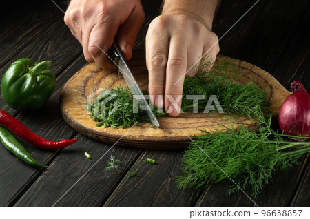 The chef cuts green dill or fennel on a cutting board with a knife for cooking vegetarian food. Peasant food. The chef cuts green dill or fennel on a cutting board with a knife for cooking vegetarian food. Peasant food. 96638857