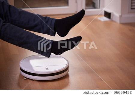Robotic vacuum cleaner cleaning the room while man sitting on sofa. Robotic vacuum cleaner cleaning the room while man sitting on sofa. 96639438