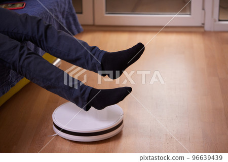 Robotic vacuum cleaner cleaning the room while man sitting on sofa. Robotic vacuum cleaner cleaning the room while man sitting on sofa. 96639439
