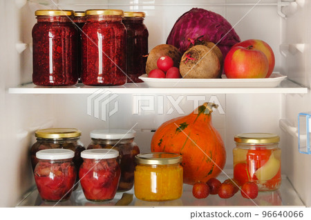 Jars with homemade fruit and berry jams and fresh red, purple and orange vegetables and fruits on shelf in fridge. Fermented healthy vegetarian foods concept. 96640066