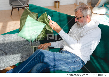Senior elderly man making online payments using laptop. Old grandfather doing shopping ecommerce with credit card. Pensioner holding debit card for internet banking. Copy space and place advertising 96640097