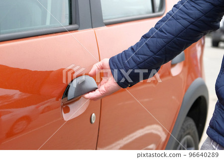 Man opens door of his orange car in parking lot. Hand on handle. Close up. 96640289