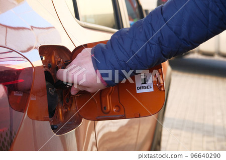 Man unscrews fuel filler cap in car. Fueling car with petrol pump at gas station. Petrol station. Diesel inscription. Close up. 96640290