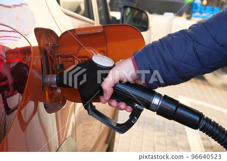 Man fills up his orange car with a gasoline at gas station. Gas station pump. To fill car with diesel fuel. 96640523