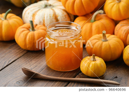 Jar of healthy pumpkin jam and wooden spoon. Pumpkins on kitchen table. 96640696