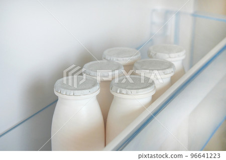 White bottles of kefir on shelf of open empty refrigerator. Fermented food concept. White bottles of kefir on shelf of open empty refrigerator. Fermented food concept. 96641223