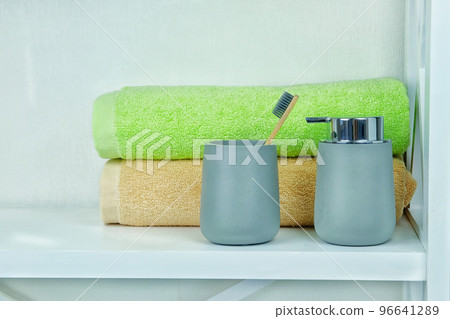 Light gray ceramic acessories for bath - soap dispenser, wooden toothbrush and towels for personal hygiene. Decor for bathroom interior. 96641289