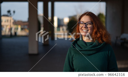 Portrait of a red-haired woman in glasses on the background of a Christmas tree outdoors.  96642316