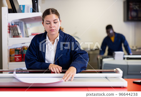 Work in printing house - woman cuts paper with professional cutter Work in printing house - woman cuts paper with professional cutter 96644238