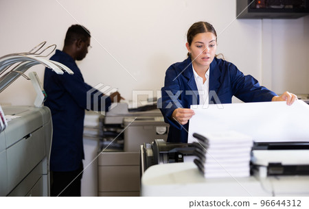 Concentrated young female in a blue robe uniform using plotter while printing a banner in the typography Concentrated young female in a blue robe uniform using plotter while printing a banner in the typography 96644312