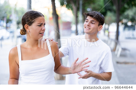Confused young woman rejecting annoying man outdoors 96644644