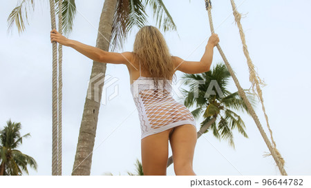 Sexual woman spends her vacation at the seaside. The girl is swinging on a swing. 96644782