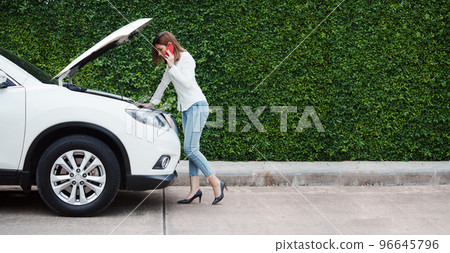 Young woman in a car broke down on the road trying to fix the problem and called a car repair shop or someone close to help. Young woman in a car broke down on the road trying to fix the problem and called a car repair shop or someone close to help. 96645796