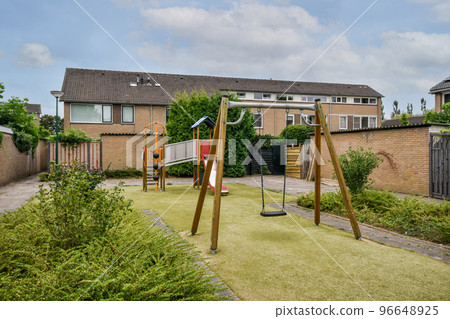 Simple small patio with small garden near playground with swings 96648925