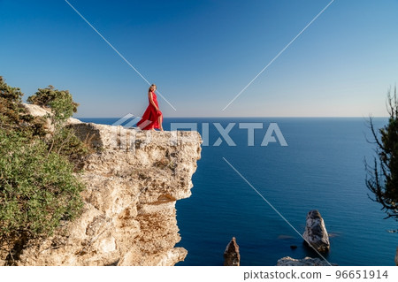 A woman in a red flying dress fluttering in the wind, against the backdrop of the sea. 96651914