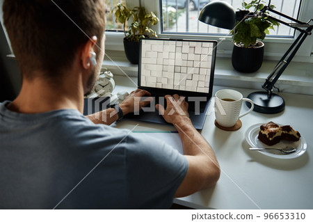 Freelancer working at home office. Man using laptop and writing in notepad sitting at table in home office 96653310