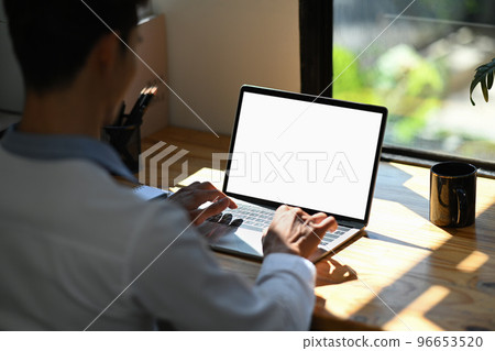 Over shoulder view of focused male office worker using laptop computer in bright office. Empty screen for advertise design Over shoulder view of focused male office worker using laptop computer in bright office. Empty screen for advertise design 96653520