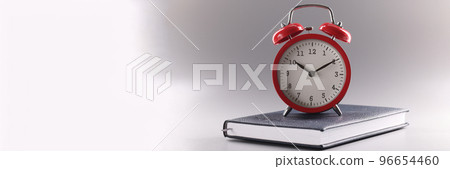 Red retro clock stand on top of closed book or diary, time to study, time to learn new information 96654460