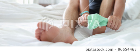 Man try to pull sock on foot, dress up to go out, sit on bed for comfort 96654465