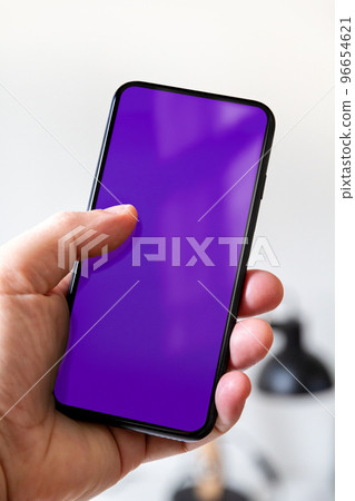 Hand holding a smartphone with blank purple screen. Office background. 96654621