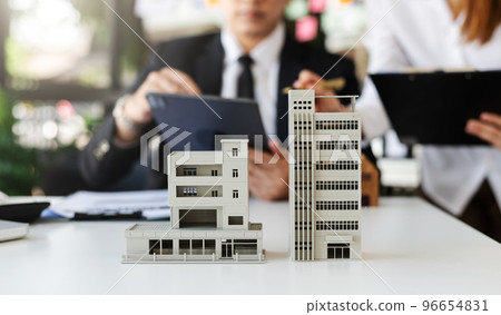 balancing the property sector The real estate agent is explaining the house style to see the house design and the purchase agreement.Wooden house at office balancing the property sector The real estate agent is explaining the house style to see the house design and the purchase agreement.Wooden house at office 96654831