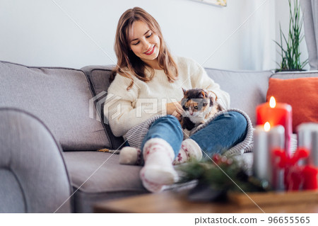 Woman in plaid with tea cup watching movie, TV, petting cat on sofa at home with christmas decoration atmosphere. Lady wear jumper and warm socks. Cozy and comfortable winter concept. Selective focus. Woman in plaid with tea cup watching movie, TV, petting cat on sofa at home with christmas decoration atmosphere. Lady wear jumper and warm socks. Cozy and comfortable winter concept. Selective focus. 96655565