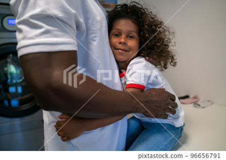 Child embracing her father at the launderette 96656791