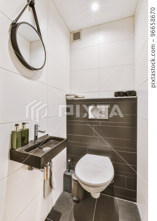 Interior of narrow restroom with sink and wall hung toilet with white walls and checkered floor 96658670