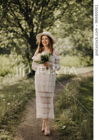 Portrait of a beautiful woman in a white dress and a hat with lilies of the valley. A girl in nature. Spring flowers Portrait of a beautiful woman in a white dress and a hat with lilies of the valley. A girl in nature. Spring flowers 96660001