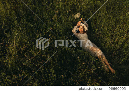 Portrait of a beautiful woman in a white dress and a hat with lilies of the valley. A girl in nature. Spring flowers Portrait of a beautiful woman in a white dress and a hat with lilies of the valley. A girl in nature. Spring flowers 96660003
