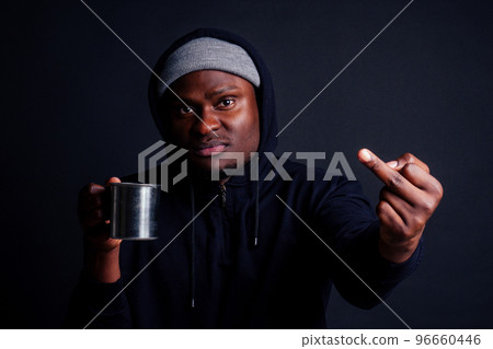 sad look african american man holding metal tourist thermos cup bad feeling.tourist alcoholic wearing gray hat and black hoody studio black background showing fuck you at camera 96660446