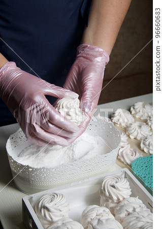 Homemade zephyr. White tray with marshmallows. A woman sprinkles marshmallows with dextrose. 96660683