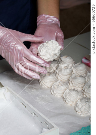 The woman will connect the halves of the marshmallow. Homemade zephyr. White tray with marshmallows. 96660729