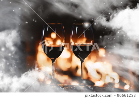 Winter atmosphere and Christmas holiday time, wine glasses in front of fireplace covered with snowy effect on window glass, holidays backgrounds 96661258