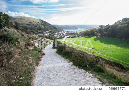 Stone road to Durdle door in Lulworth, part of Jurassic Coast World Heritage Site, view of the seaside cottages and Lulworth Cove in the background, selective focus Stone road to Durdle door in Lulworth, part of Jurassic Coast World Heritage Site, view of the seaside cottages and Lulworth Cove in the background, selective focus 96663771