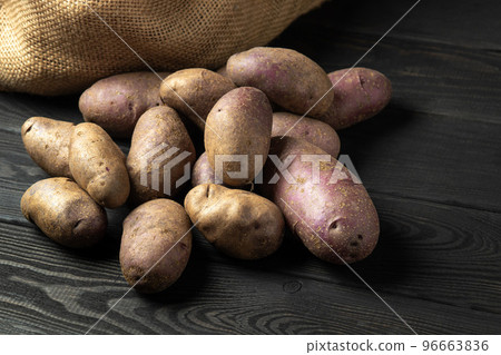 Bunch of potatoes after harvest lying on black wooden boards with a potato sack in the background 96663836