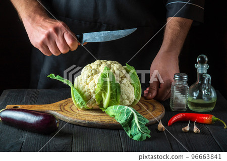 Cook is cutting cauliflower in a restaurant kitchen. The idea of a delicious diet for breakfast or dinner Cook is cutting cauliflower in a restaurant kitchen. The idea of a delicious diet for breakfast or dinner 96663841