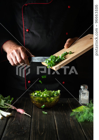 Adding chopped green onions to a fresh vegetable salad. Chef while cooking delicious food in the kitchen Adding chopped green onions to a fresh vegetable salad. Chef while cooking delicious food in the kitchen 96663886