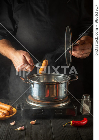 Cook cooks Vienna sausage in a saucepan. Working environment in the restaurant kitchen. Delicious breakfast or dinner Cook cooks Vienna sausage in a saucepan. Working environment in the restaurant kitchen. Delicious breakfast or dinner 96663917