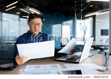 Asian businessman not satisfied with achievement results, boss looking at documents and upset, man in glasses and shirt working inside office with paperwork using laptop. Asian businessman not satisfied with achievement results, boss looking at documents and upset, man in glasses and shirt working inside office with paperwork using laptop. 96663930