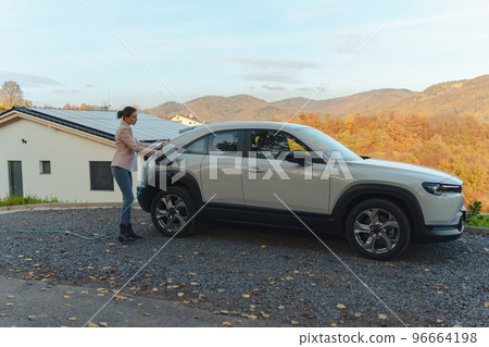 Young woman charging her electric car in home, sustainable and economic transportation concept. 96664198