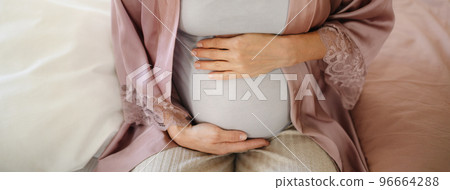 Close-up of pregnant woman stroking her belly, sitting on bed. Close-up of pregnant woman stroking her belly, sitting on bed. 96664288