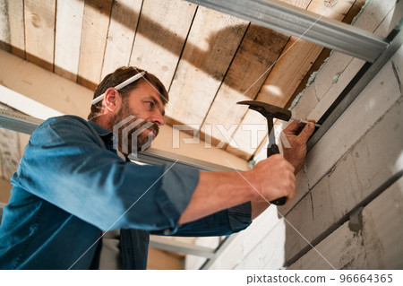 Mature handyman driving a nail in unfinished house construction, diy concept. 96664365